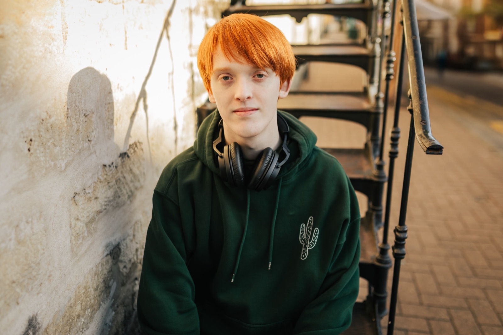 Kade Jackson, the producer behind prickly, sitting on a fire escape in a forest-green hoodie